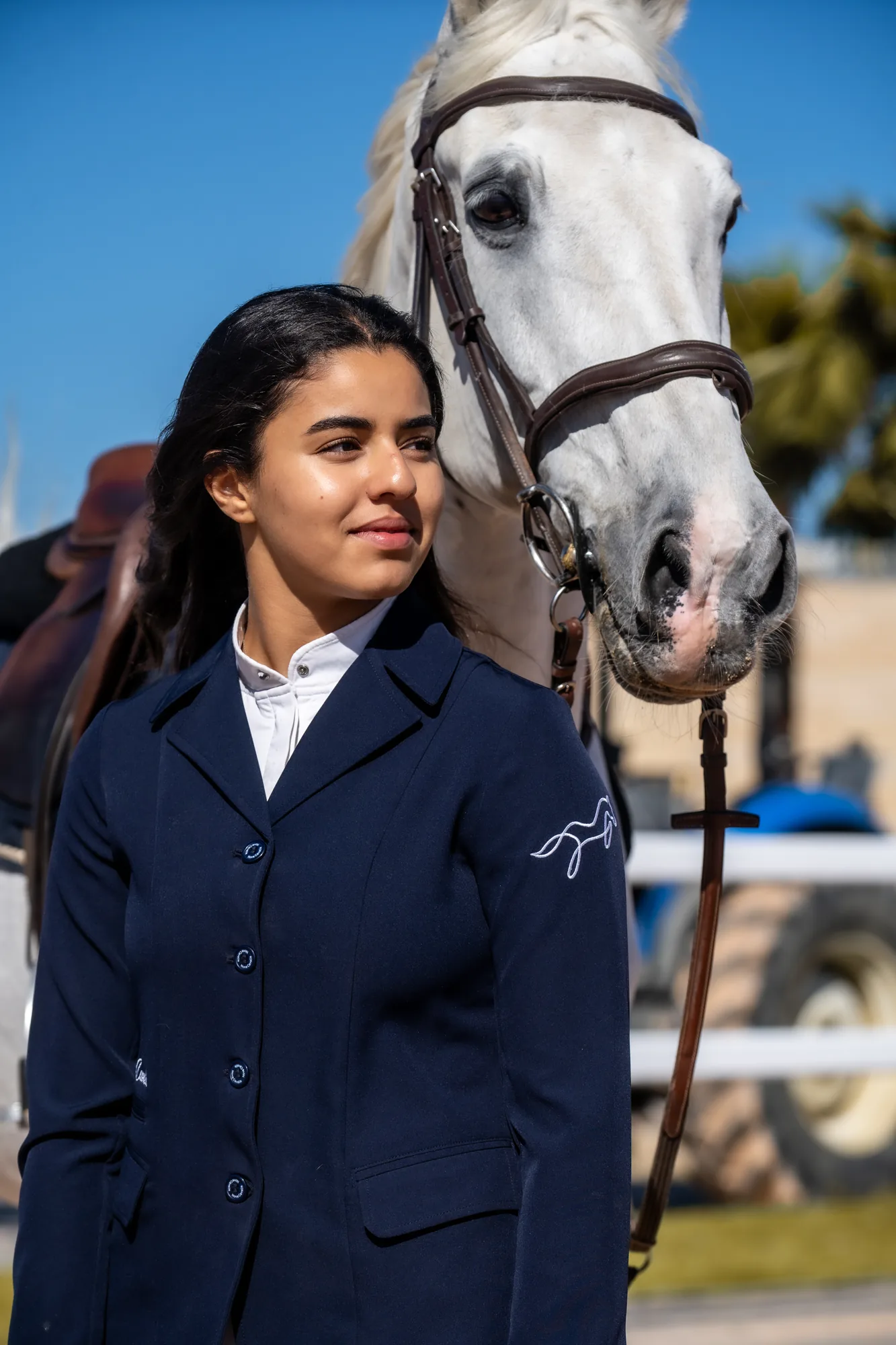 Cavaliere en veste de concours marine devant un cheval gris